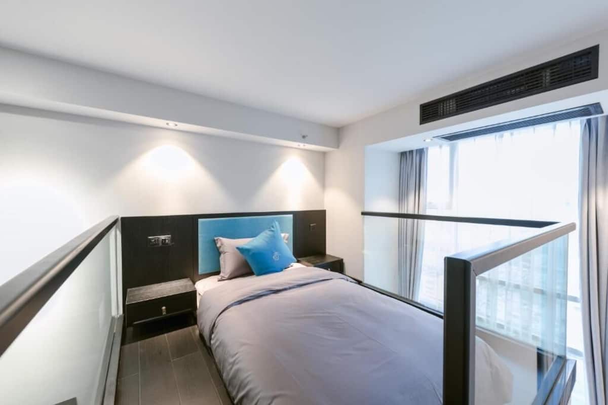 A modern hotel room with a bed, a nightstand, a window with curtains, and a view of the city.