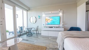Une chambre d’hôtel moderne dotée d’une grande télévision, d’un lit, d’un coin salon avec des fauteuils et offrant une vue à travers la porte vitrée.