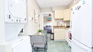 Une cuisine compacte équipée d’un lave-linge, un coin repas avec une table et des chaises, et une vue sur une chambre.