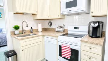 A compact kitchen with a microwave, stove, dishwasher, and coffee maker.