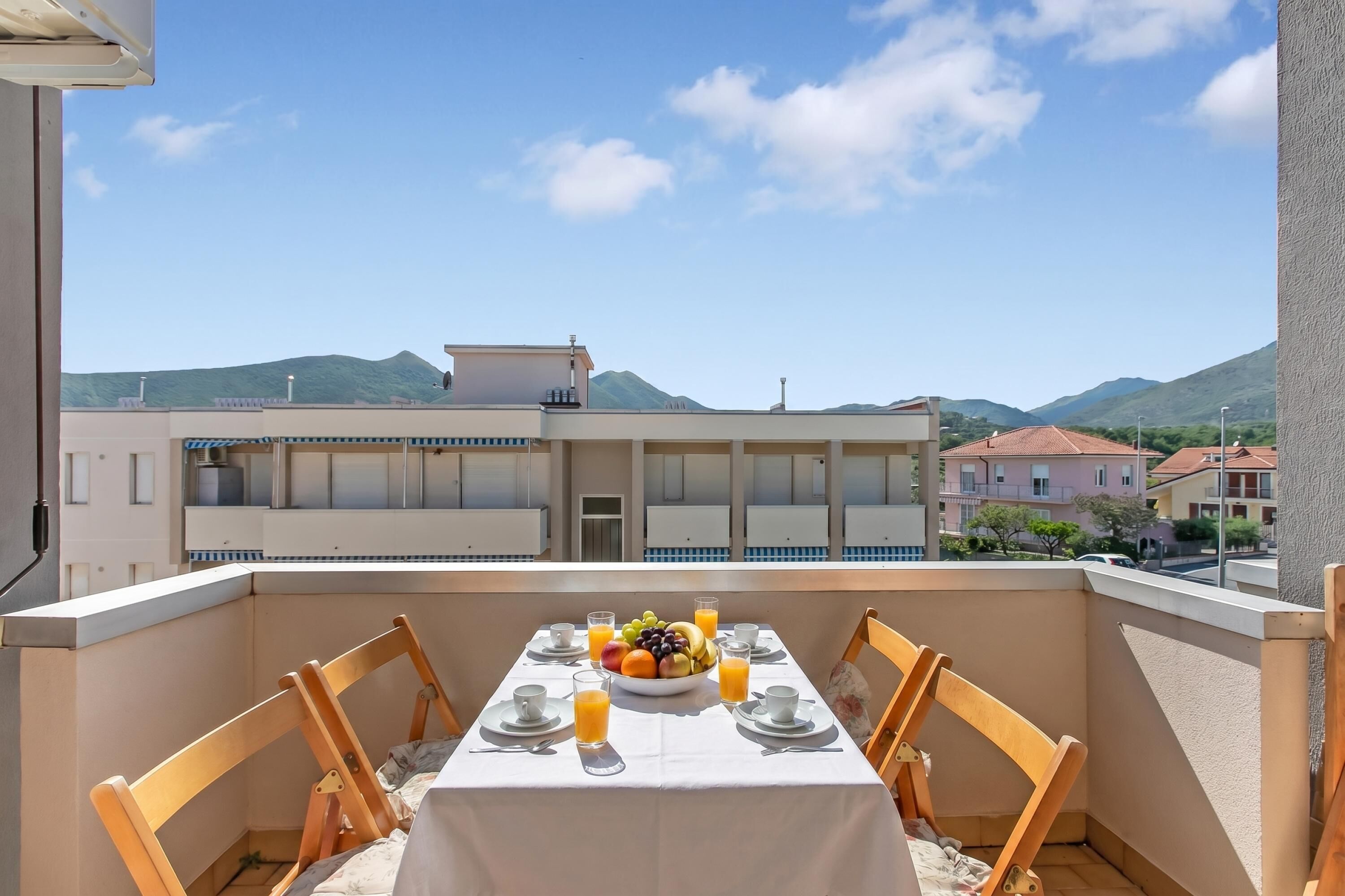Ein Balkon mit einem für das Frühstück gedeckten Tisch, einer Obstschale und Gläsern Orangensaft.