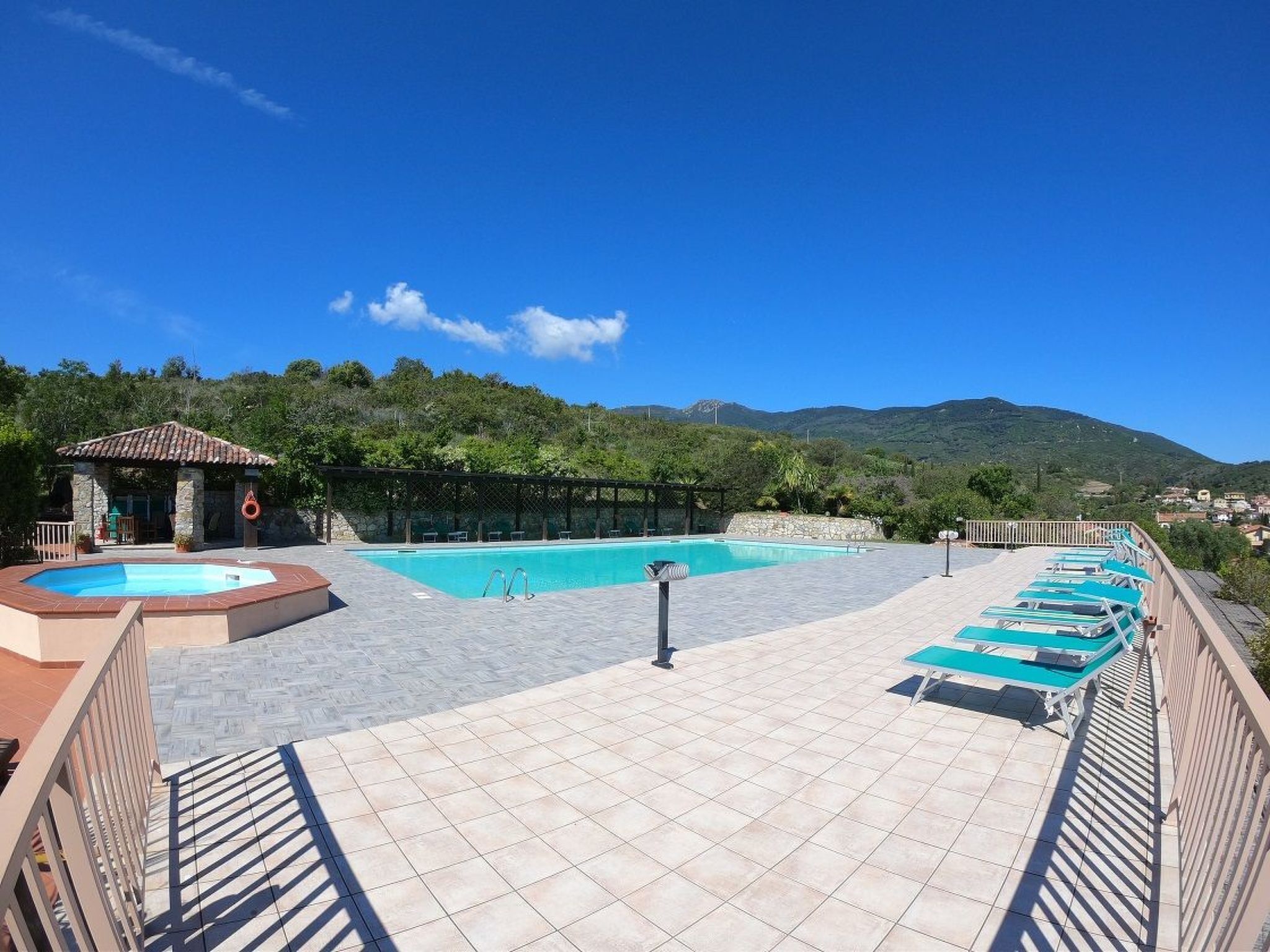A pool area with a hot tub, lounge chairs, and a pergola.