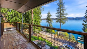 A wooden deck with a metal railing overlooking a lake with trees and a distant mountain range. - Hayden Lake Oasis | Private Dock and Boat Slip | Fire Pit and Lake Access (Hayden)