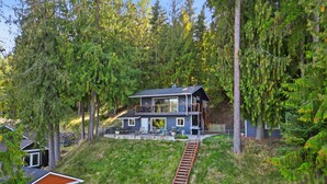 A modern two-story house with a balcony, surrounded by dense forest. - Hayden Lake Oasis | Private Dock and Boat Slip | Fire Pit and Lake Access (Hayden)