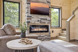 Un salon chaleureux avec une cheminée en pierre, un téléviseur à écran plat et un canapé confortable.