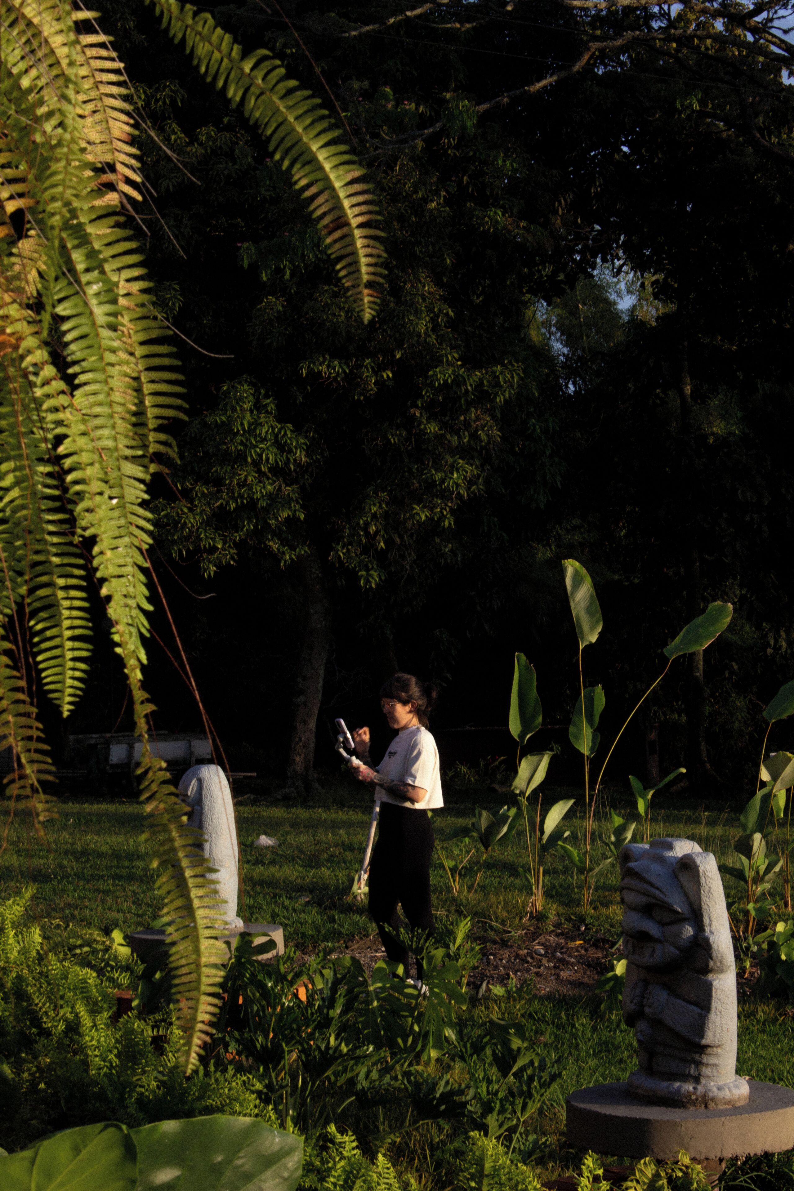 Uma pessoa em um jardim com uma estátua de pedra e samambaias.