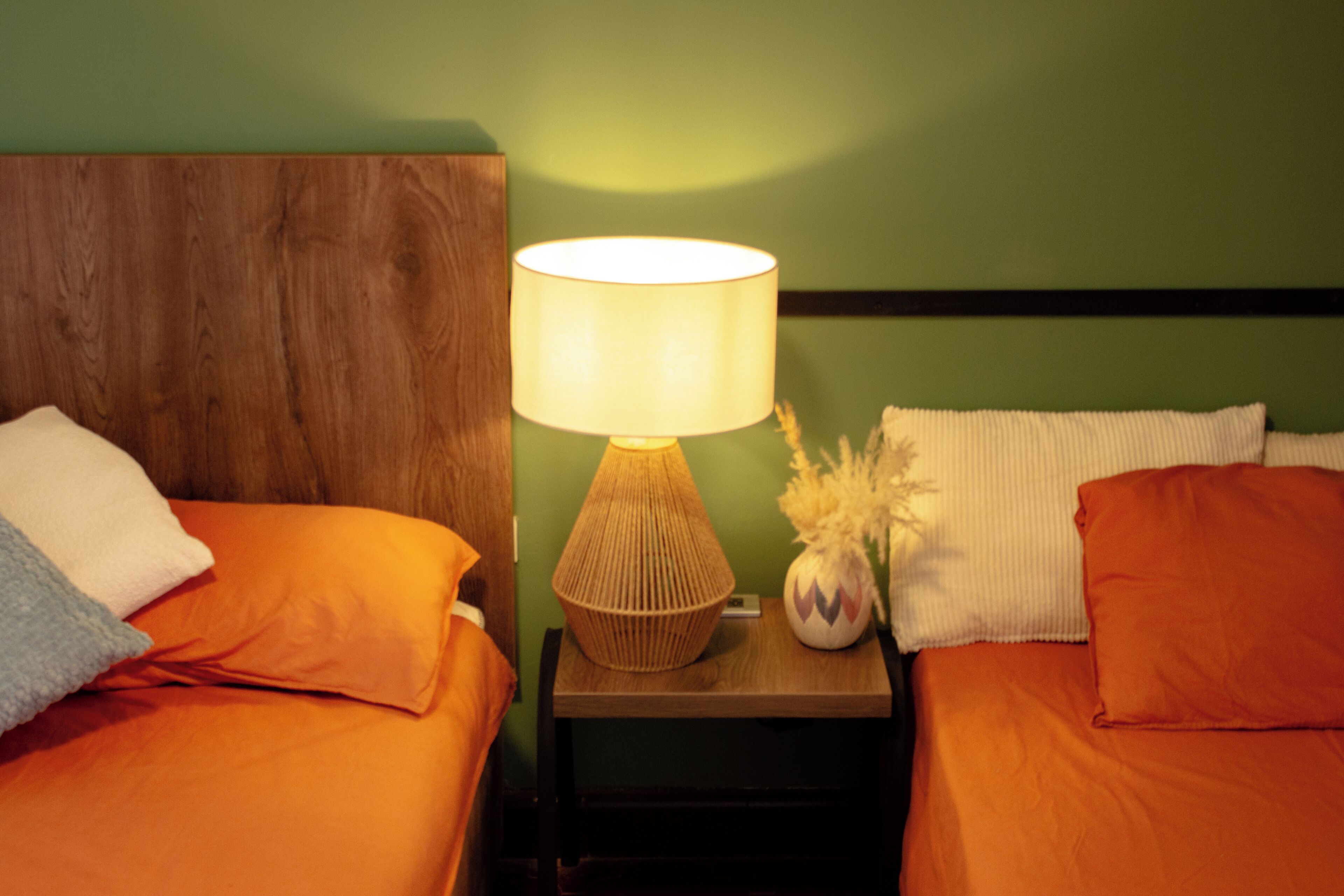 Ein Zimmer mit zwei Betten, einem Nachttisch mit Lampe und einer Vase mit getrockneten Blumen.