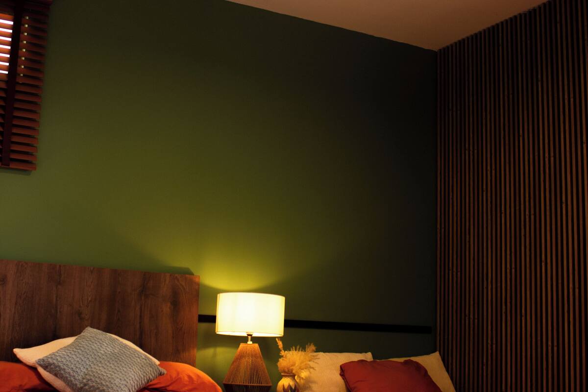 A bedroom with a bed, a ceiling fan, a nightstand with a lamp, and a wall with vertical lines.