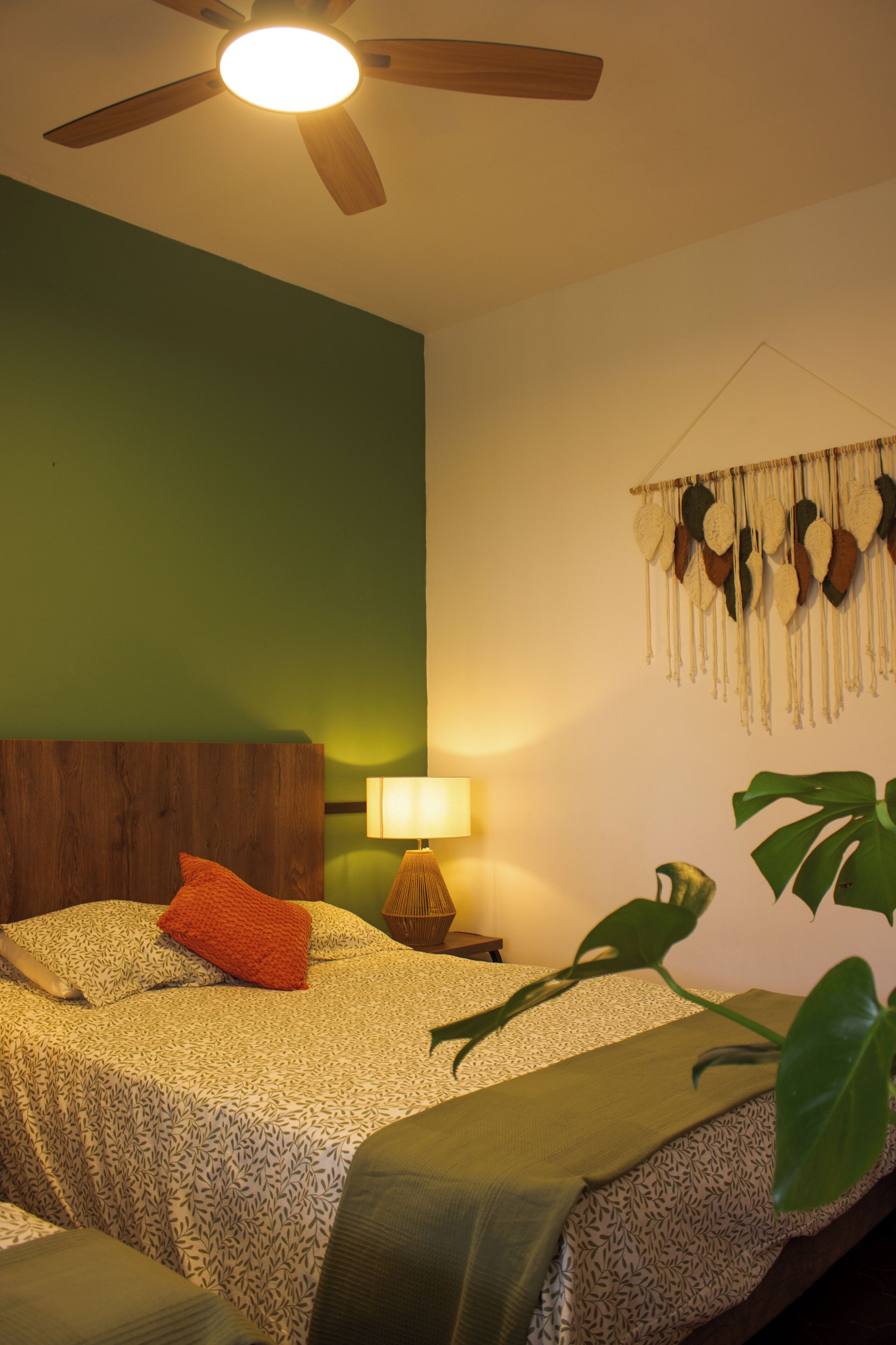 Ein Schlafzimmer mit einem Bett, einem Deckenventilator, einer Wandlampe und einem Wandbehang aus Makramee.