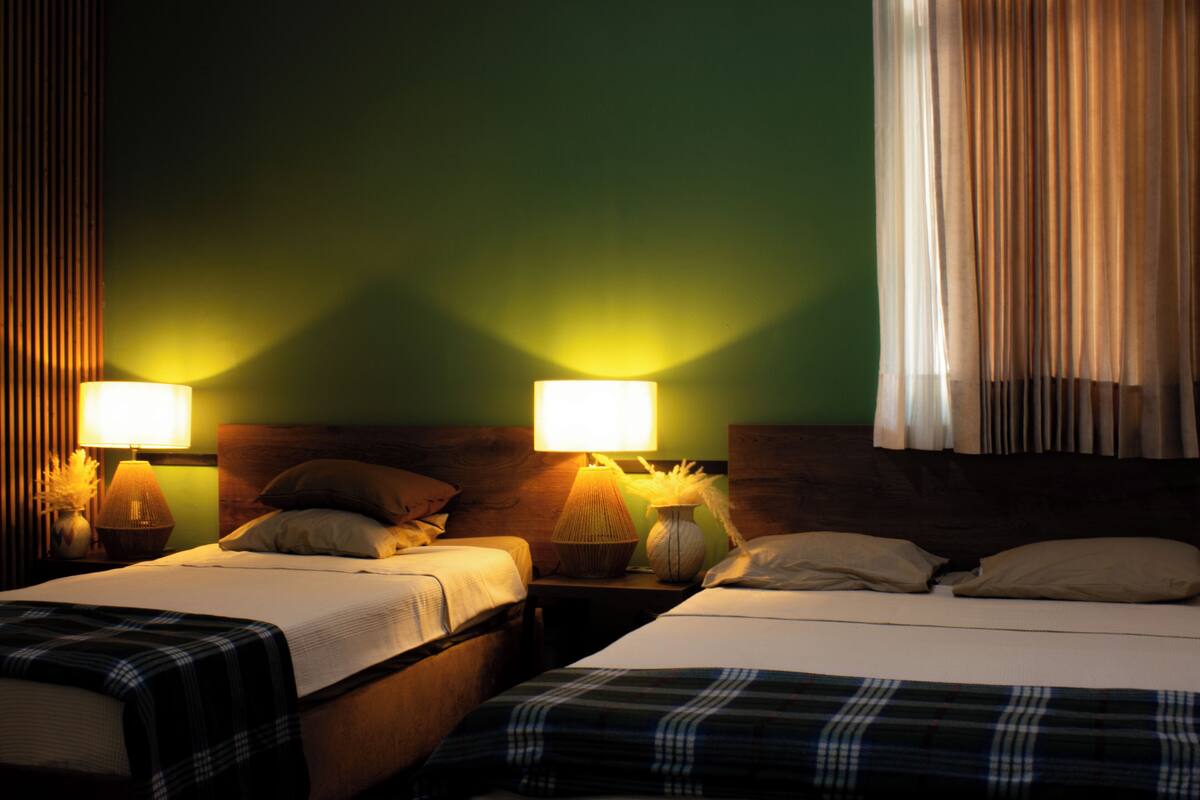 A hotel room with two beds, nightstands with lamps, a vase with flowers, and a curtain.