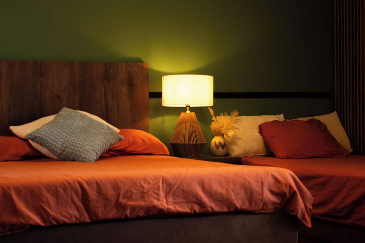 A bed with a wooden headboard, a bedside lamp, and multiple pillows.
