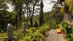 A garden pathway with statues, lush greenery, and a stone wall. - Alma Terra Campestre (Ginebra)