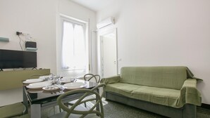 A room with a dining table set for four, a green sofa, a TV, and a window with curtains. - 1 bedroom nice apartment in Genova (Genova)