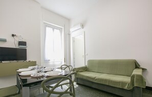 Ein Zimmer mit Esstisch für vier Personen, einem grünen Sofa, einem Fernseher und einem fenster mit Vorhängen.