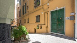 A narrow street with a yellow building, a green door, and a small garden area. - 1 bedroom nice apartment in Genova (Genova)