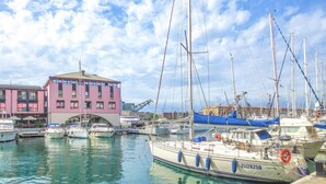A marina with several boats docked, a building with pink and purple facades, and a clear blue sky. - 1 bedroom nice apartment in Genova (Genova)