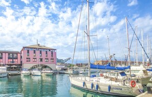 Ein Yachthafen mit mehreren vertäuten Booten, ein Gebäude mit rosa und violetten Fassaden und einem strahlend blauen Himmel.