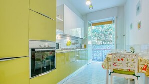 Eine Küche mit einem gelben Kühlschrank, weißen Schränken, einem Doppelbackofen und einem Essbereich mit Tisch und Stühlen.