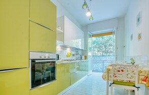 Eine Küche mit einem gelben Kühlschrank, weißen Schränken, einem Doppelbackofen und einem Essbereich mit Tisch und Stühlen.