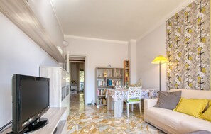 Ein Wohnzimmer mit Fernseher, einer Couch, einem Tisch und einem Bücherregal.