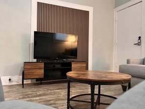 Ein modernes Wohnzimmer mit Flachbildfernseher, Holzunterhaltungseinheit, rundem Couchtisch und grauem Sofa.