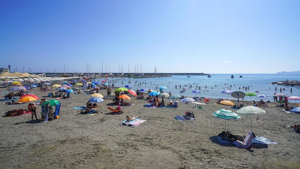 Ein Strand mit vielen Sonnenschirmen und liegebaden Personen.