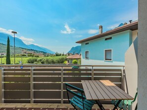 Ein Balkon mit Tisch und Stühlen, der auf eine gebirgige Landschaft mit Häusern und viel Grün blickt.