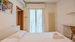 A hotel room with a bed, a window with curtains, a radiator, and a wall-mounted air conditioning unit. - Riva Olive by Interhome (Riva del Garda)