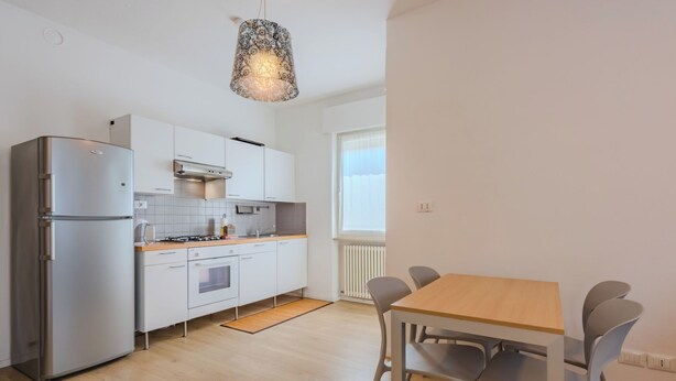 A modern kitchen with white cabinets, a stainless steel refrigerator, and a wooden dining table with chairs. - Riva Olive by Interhome (Riva del Garda)