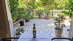 Eine Terrasse mit Tisch für Zwei, Blumentöpfen und einer Weinflasche.