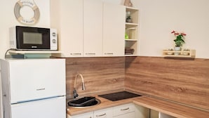 Eine kleine Küche mit weißen Schränken, einer Holzrückwand, einer eingebauten Mikrowelle und einem Spülbecken mit Armatur.