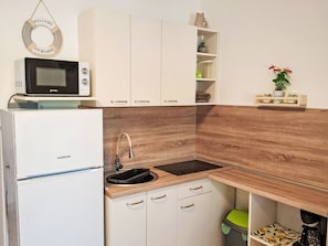 A compact kitchen with white cabinets, a wooden backsplash, a built-in microwave, and a sink with a faucet. - Gemütliches Erdgeschoss-Studio für 2 Personen by Interhome (Crikvenica)