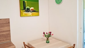Ein Essbereich mit Tisch, Stühlen, einer Vase mit Blumen, einem Gemälde und einer Uhr an der Wand.
