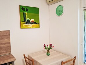 A dining area with a table, chairs, a vase with flowers, a painting, and a clock on the wall. - Gemütliches Erdgeschoss-Studio für 2 Personen by Interhome (Crikvenica)