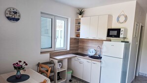 Uma cozinha compacta com mesa de jantar, micro-ondas, geladeira e janela com persianas.
