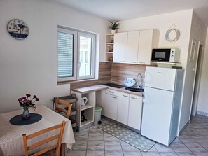 Eine kompakte Küche mit Esstisch, Mikrowelle, Kühlschrank und einem Fenster mit Jalousien.