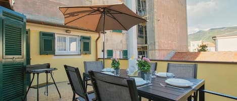 A dining area with a table set for two, outdoor chairs, a table umbrella, and potted plants.