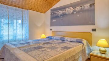 Una camera da letto con soffitto in legno, un letto con copriletto decorato, due lampade ai comodini e un grande dipinto raffigurante un paesaggio sulla parete.