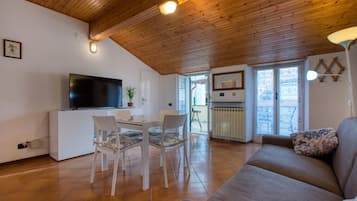 Un soggiorno con soffitto in legno, televisore, tavolo da pranzo con sedie, divano e termosifone.