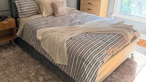 A bedroom with a bed, a nightstand, a dresser, a wall-mounted air conditioner, and a window with blinds.