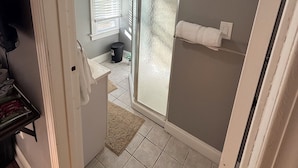 A bathroom with a glass shower door, a towel rack, and a window with blinds.