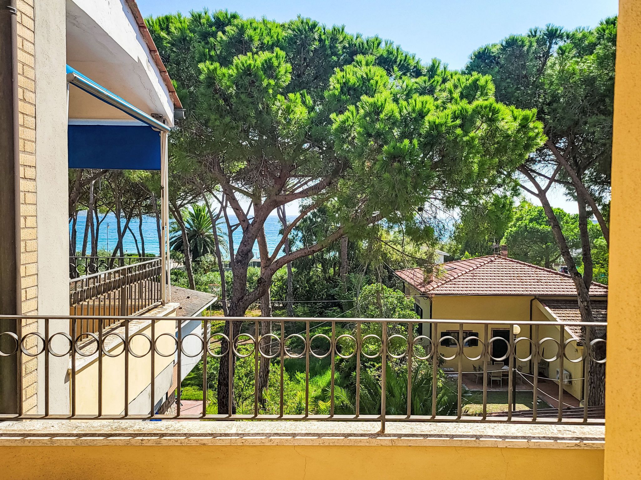 A balcony with a view of a coastal area, a building with a blue and white facade, and a yellow wall.