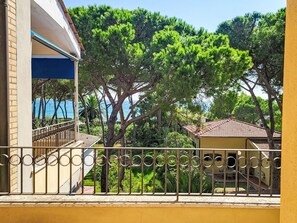 Ein Balkon mit Blick auf eine Küstenlandschaft, ein Gebäude mit blau-weißer Fassade und einer gelben Wand.