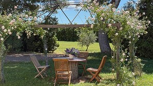 Un jardin agrémenté d’une pergola, de chaises en bois et d’une table décorée de fleurs.