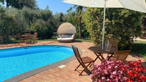 Une piscine avec un parasol, des chaises longues et une table avec des chaises.