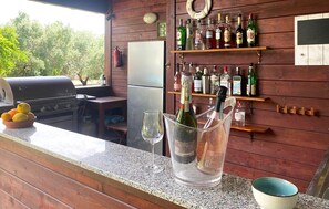 Eine Barbereich mit Grill, Kühlschrank und einer Auswahl an Spirituosenflaschen in Regalen.