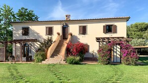 Une maison à deux étages avec un escalier central, une pergola et une pelouse bien entretenue.