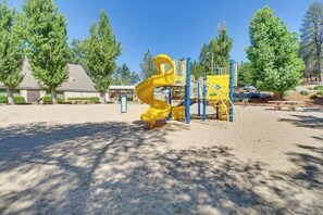 Ein Spielplatz mit einer gelben Rutsche und Klettergerüsten, umgeben von Bäumen und einem Gebäude im Hintergrund.