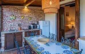 Une cuisine avec un mur en briques, un four à micro-ondes, un réfrigérateur et une table recouverte d’une nappe bleue et jaune.