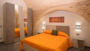 Una camera da letto con un arco in pietra, un letto con copriletto arancione, uno specchio e due luci a parete.